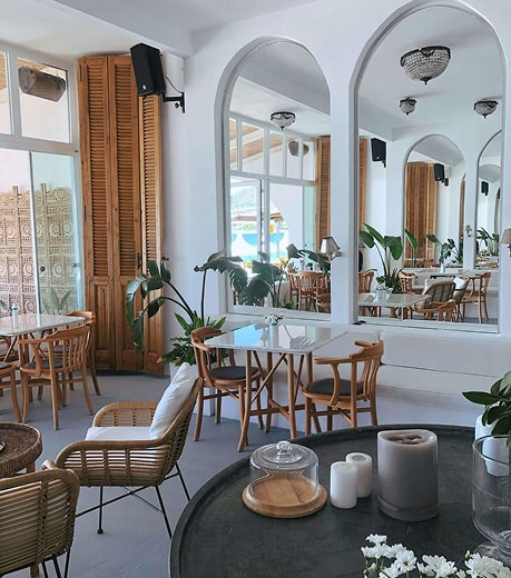 Intérieur moderne d'une boulangerie avec miroirs cintrés, tables en bois, chaises en rotin, plantes vertes et comptoir noir