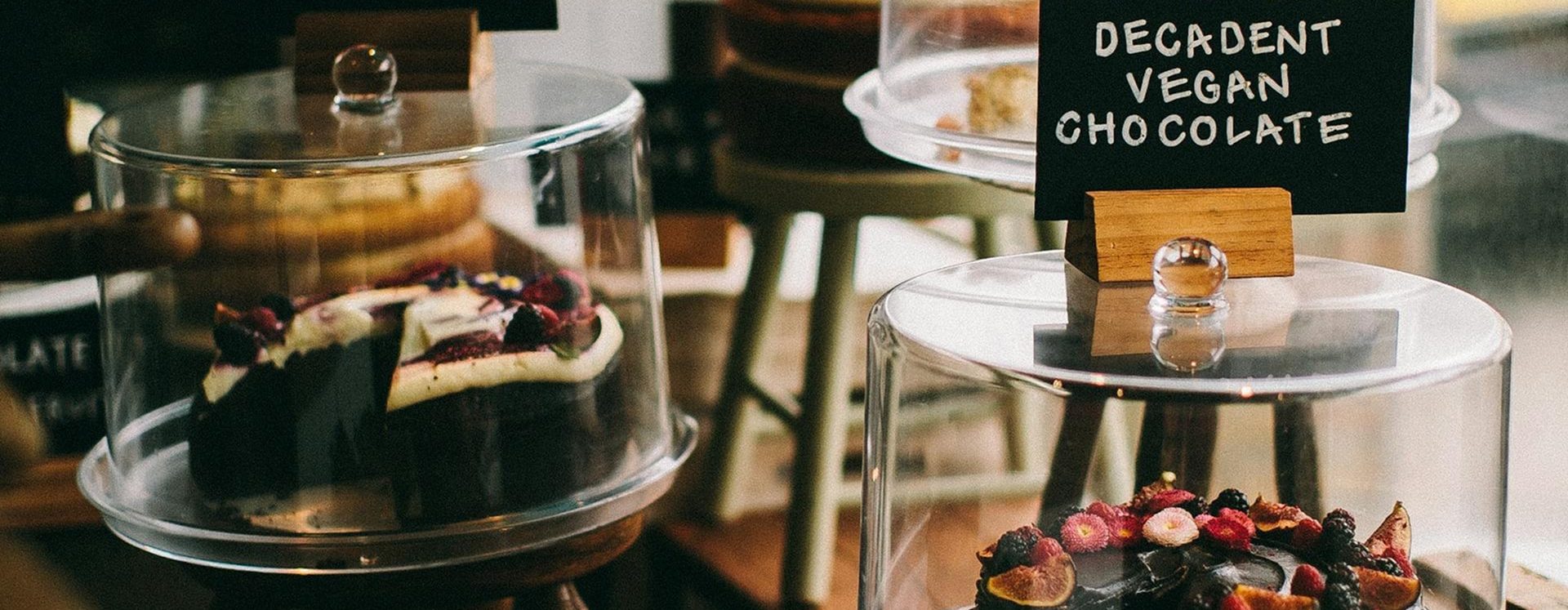 Vitrine de pâtisserie avec gâteau au chocolat végan sous cloche en verre, garni de fruits rouges et frais