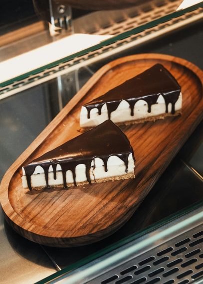 Deux parts de cheesecake avec glaçage au chocolat noir dégoulinant sur planche en bois ovale