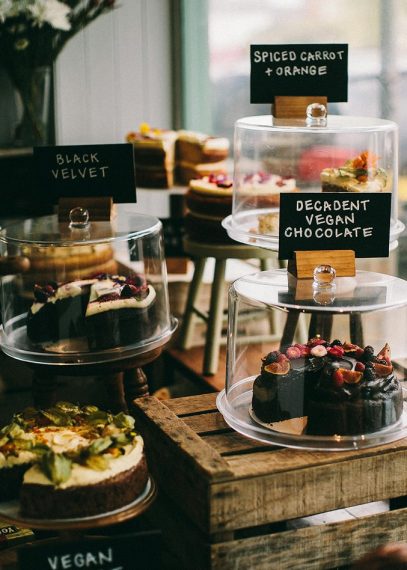 Vitrine de pâtisseries artisanales sous cloche avec étiquettes noires : gâteau Black Velvet, Decadent Vegan Chocolate et