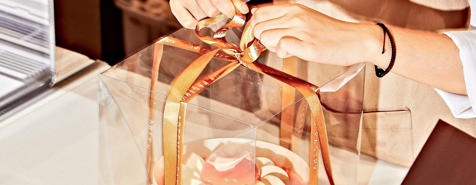 Mains ouvrant un emballage transparent avec ruban doré d'une pâtisserie artisanale