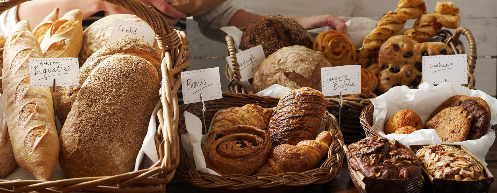 Assortiment de pains et pâtisseries artisanales dans des paniers en osier avec étiquettes: baguettes, pains complets