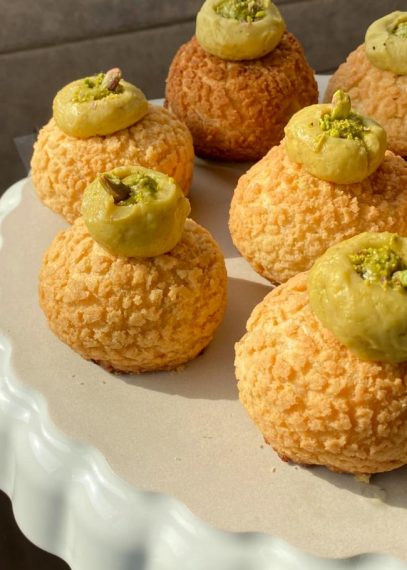 Pâtisseries rondes dorées avec glaçage vert pistache sur plateau blanc, décorées de pistaches concassées