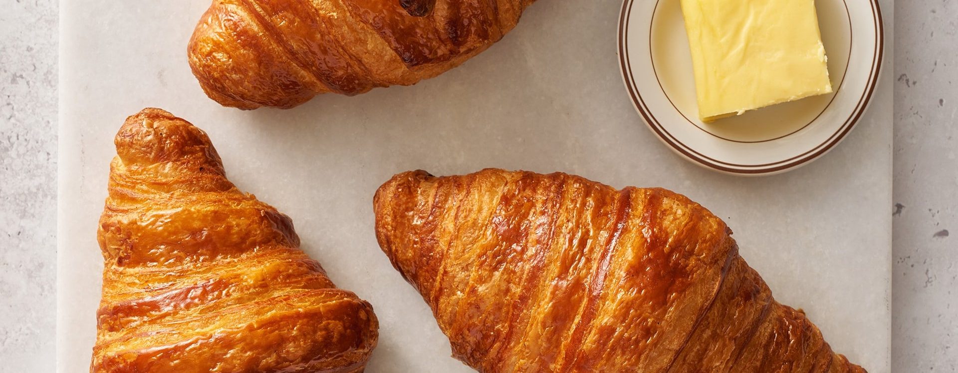 Trois croissants dorés et croustillants avec du beurre frais dans un bol en verre sur fond clair