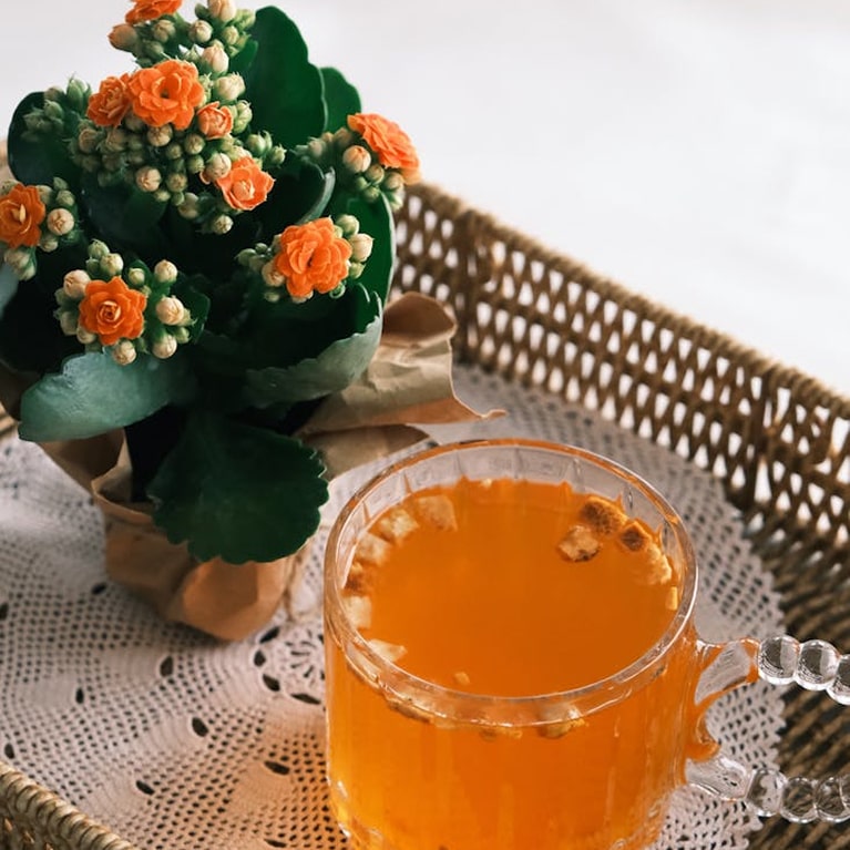 Jus d'orange frais et fleurs oranges Un verre de jus d'orange frais à côté d'une plante avec fleurs orange en pot, sur une nappe blanche avec panier en
