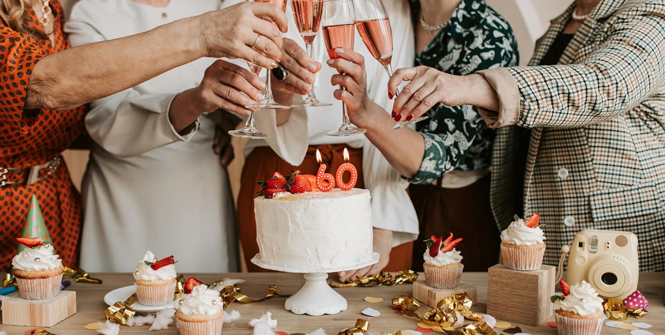 Groupe de personnes trinquant avec des verres de champagne rosé autour d'un gâteau blanc orné de bougies numérotées 80 et