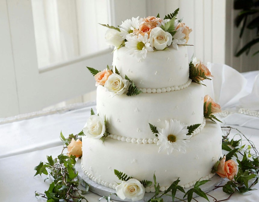 Gâteau de mariage trois étages blanc avec roses pêche, marguerites blanches et perles décoratives