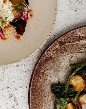 Assiettes de céramique texturée avec légumes rôtis, herbes fraîches et fleurs comestibles sur surface blanche