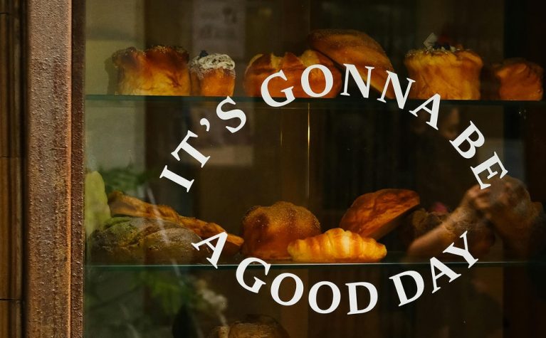 Vitrine de boulangerie avec pains dorés et pâtisseries fraîchement cuites, texte 'It's gonna be a good day' sur la vitre