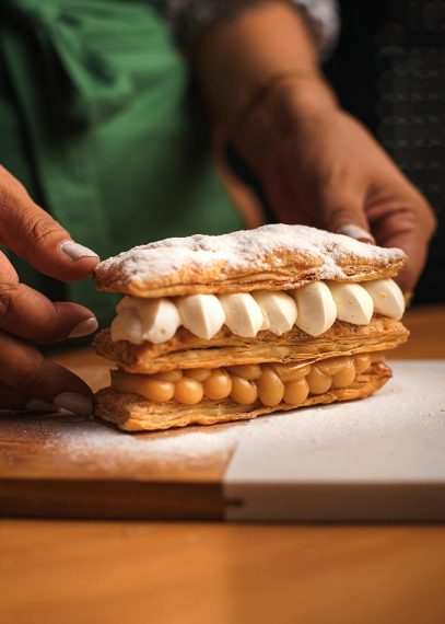 Main tenant un éclair pâtissier feuilleté garni de crème blanche et perles de sucre dorées