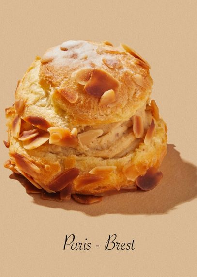Paris-Brest, pâtisserie française avec choux dorés, amandes effilées et sucre glace sur fond beige
