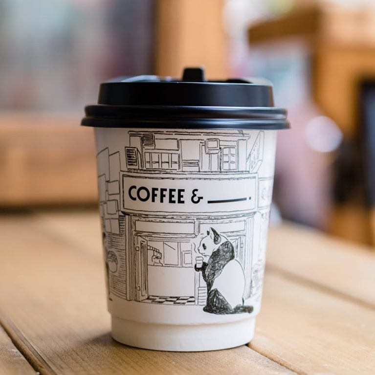 Gobelet Coffee & avec mascotte panda - Sugar Town Gobelet de café blanc avec couvercle noir, illustration d'une panda dans un café et texte Coffee & sur fond en bois