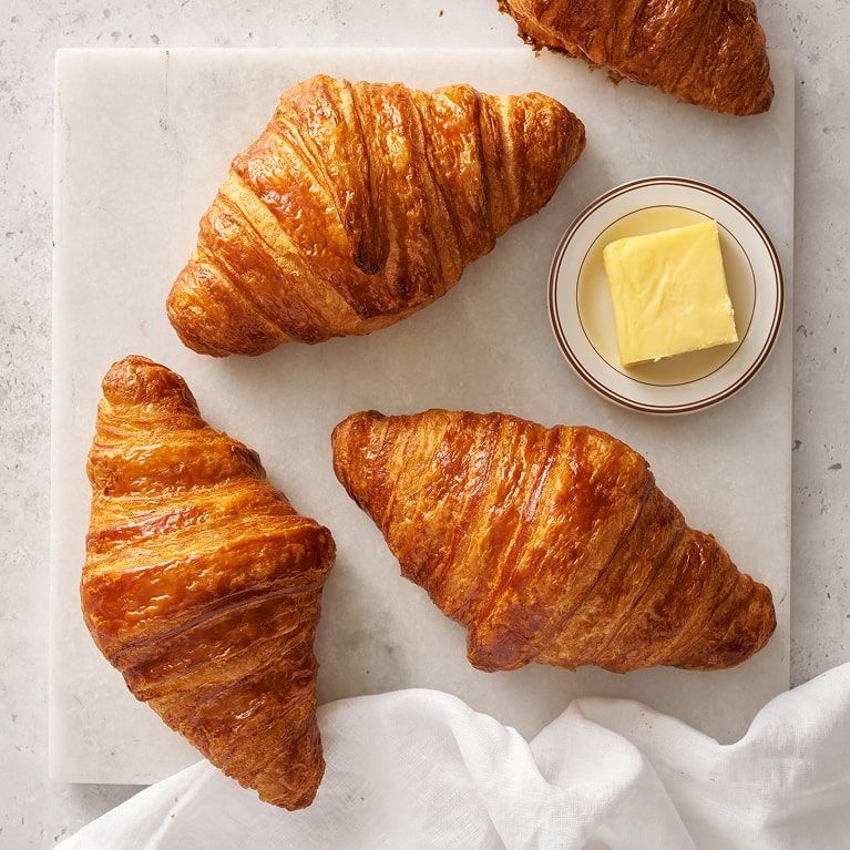 Croissants frais et beurre artisanal du programme rewards Trois croissants dorés et beurrés disposés sur papier blanc avec un petit bol de beurre frais