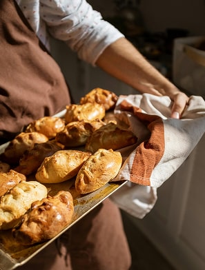Boulanger présentant un plateau de croissants dorés fraîchement sortis du four, enveloppés dans du papier blanc