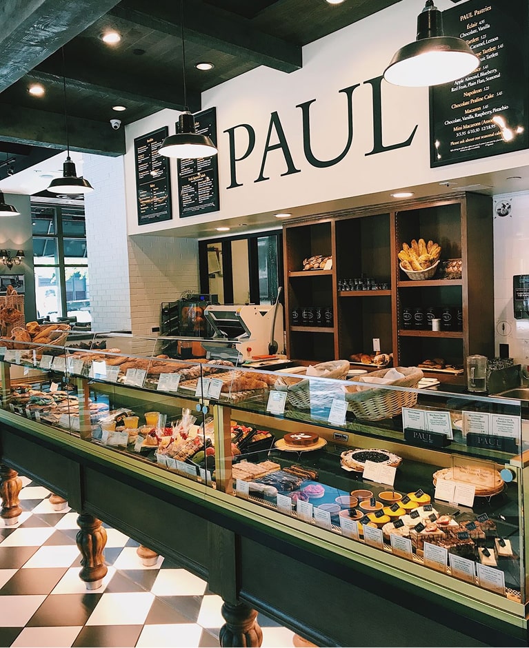 Boulangerie Paul avec vitrines de pains artisanaux, pâtisseries et sandwiches, comptoir vert et noir, décor blanc et moderne