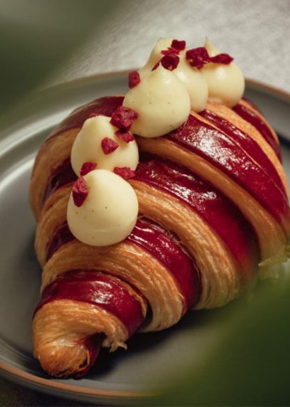 Croissant feuilleté garni de coulis rouge et surmonté de boules de mousse blanche parsemées de fruits rouges