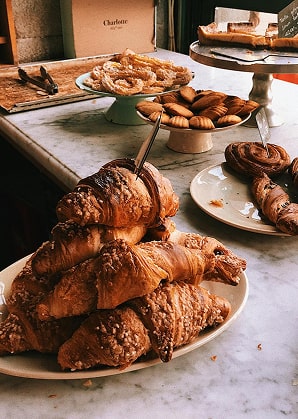Plateau de croissants et gaufres de Liège dorés disposés sur un comptoir en marbre blanc avec d'autres pâtisseries en