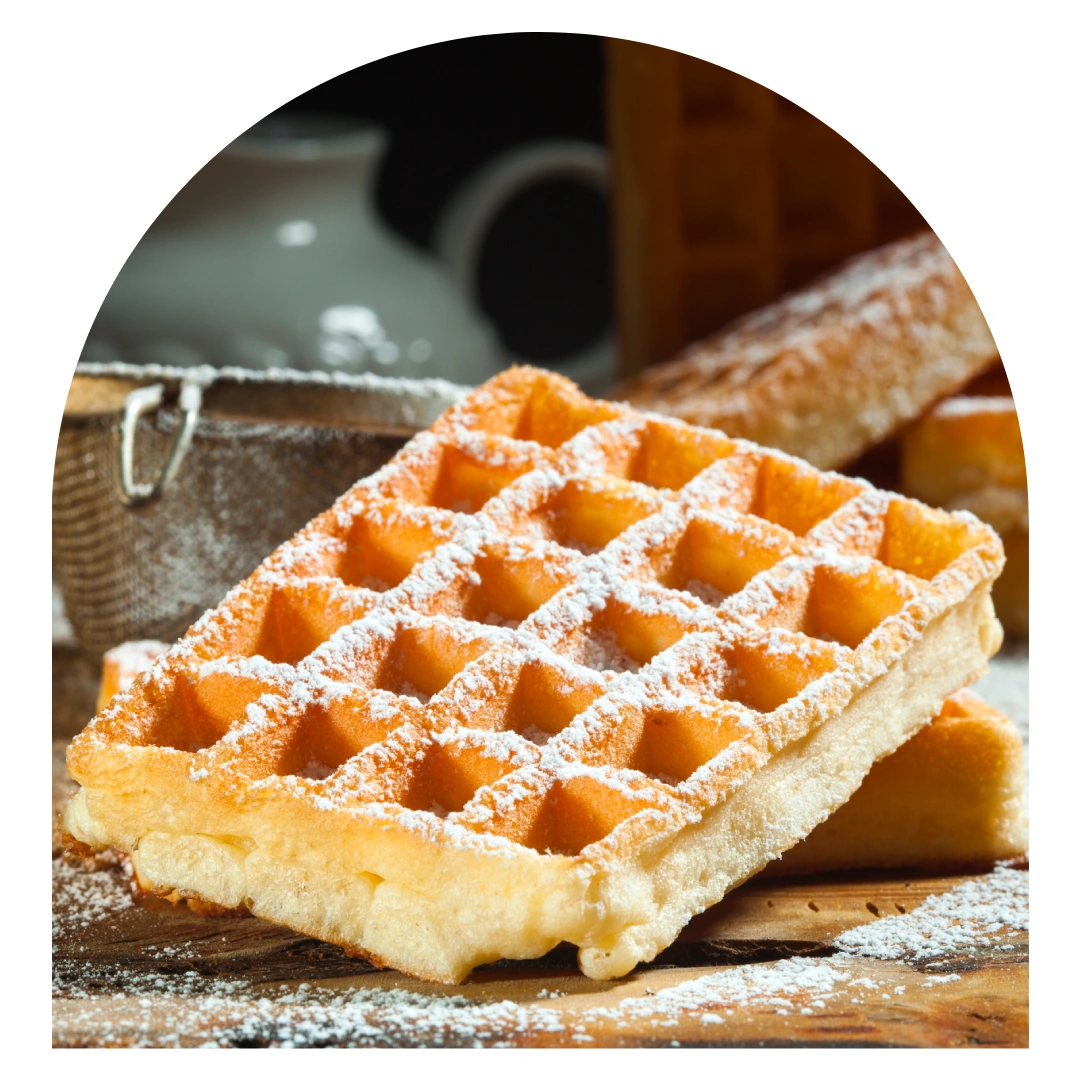Gaufre de Liège artisanale saupoudrée de sucre blanc, posée sur du bois avec un panier en arrière-plan