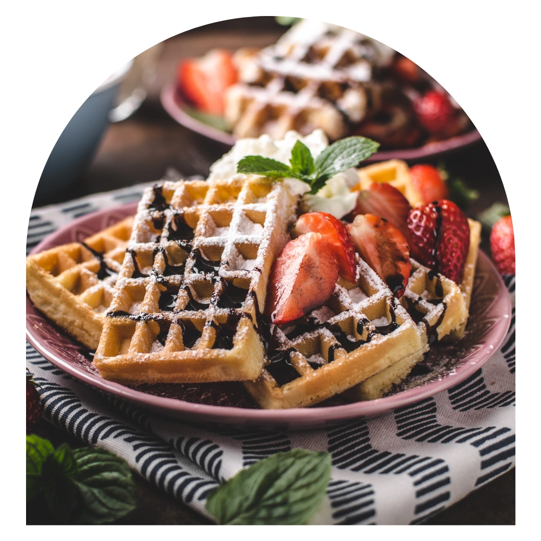 Gaufres de Liège saupoudrées de sucre glace garnies de fraises fraîches et crème blanche sur assiette rose
