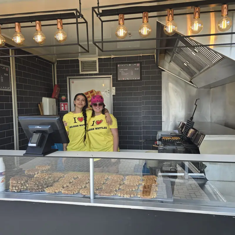 Deux employées souriantes en t-shirts jaunes Mister Wafer devant un comptoir de vente de gaufres de Liège, avec affichage