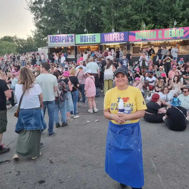 Femme en t-shirt jaune et jupe bleue souriante à un événement festif avec food truck affichant Loempia's Koffie Wafels et