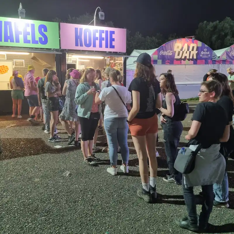 Queue devant un stand de koffie et gaufres lors d'une fête foraine nocturne avec plusieurs clients attendant