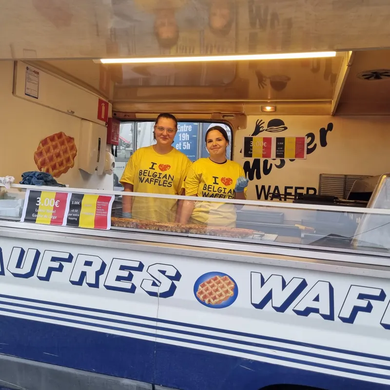 Deux vendeurs en t-shirt jaune I love Belgian Waffles derrière le comptoir d'une boutique de gaufres de Liège Mister Wafer