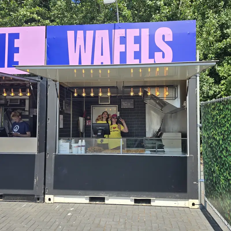 Food truck Wafels avec deux employées en uniforme jaune servant des gaufres, abreuvoir doré, signalétique bleue et rose