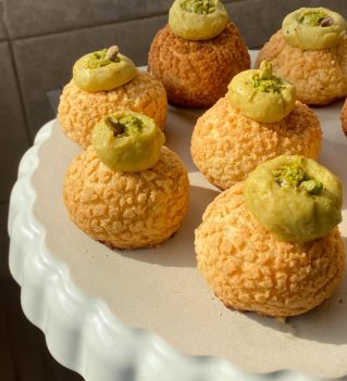 Pâtisseries rondes dorées avec glaçage vert pistache sur plateau blanc, décorées de pistaches concassées
