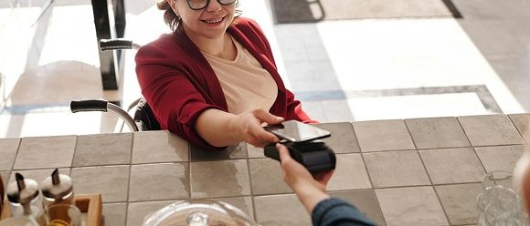 Femme avec lunettes en chemise rouge effectuant un paiement sans contact avec un portefeuille numérique sur terminal de